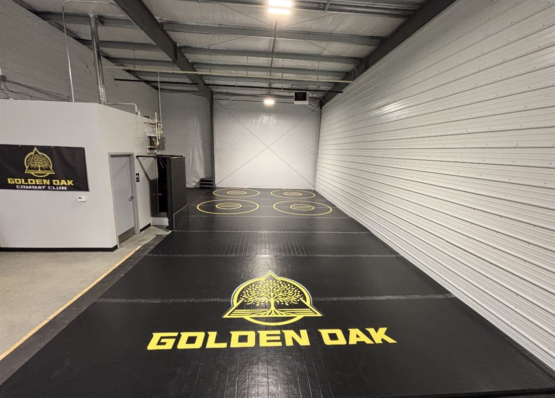 The Golden Oak Combat Club mat room — clean black wrestling mats with the gold oak logo